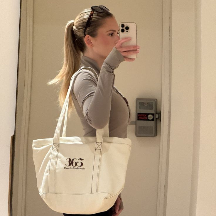 Person taking a mirror selfie with a beige tote bag featuring '365' branding.