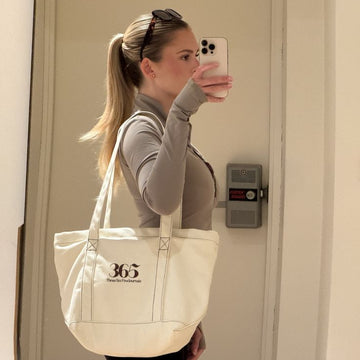 Person taking a mirror selfie with a beige tote bag featuring '365' branding.