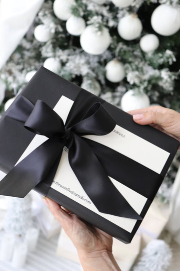 hands holding a gift wrapped journal with black ribbon in front of a Christmas tree