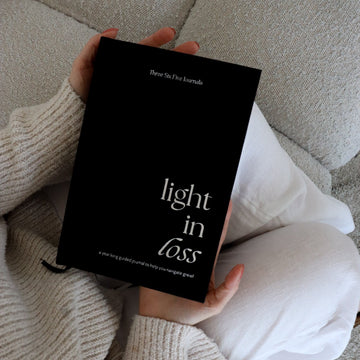 Person holding a book titled 'Light in Loss' on a couch